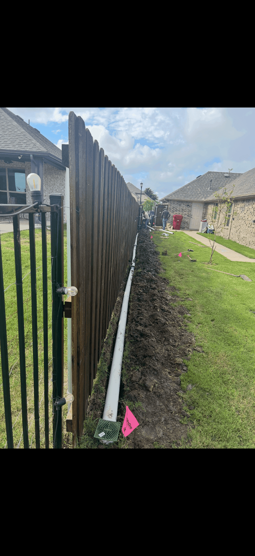 French drain installation along a fence line to route water through the yard
